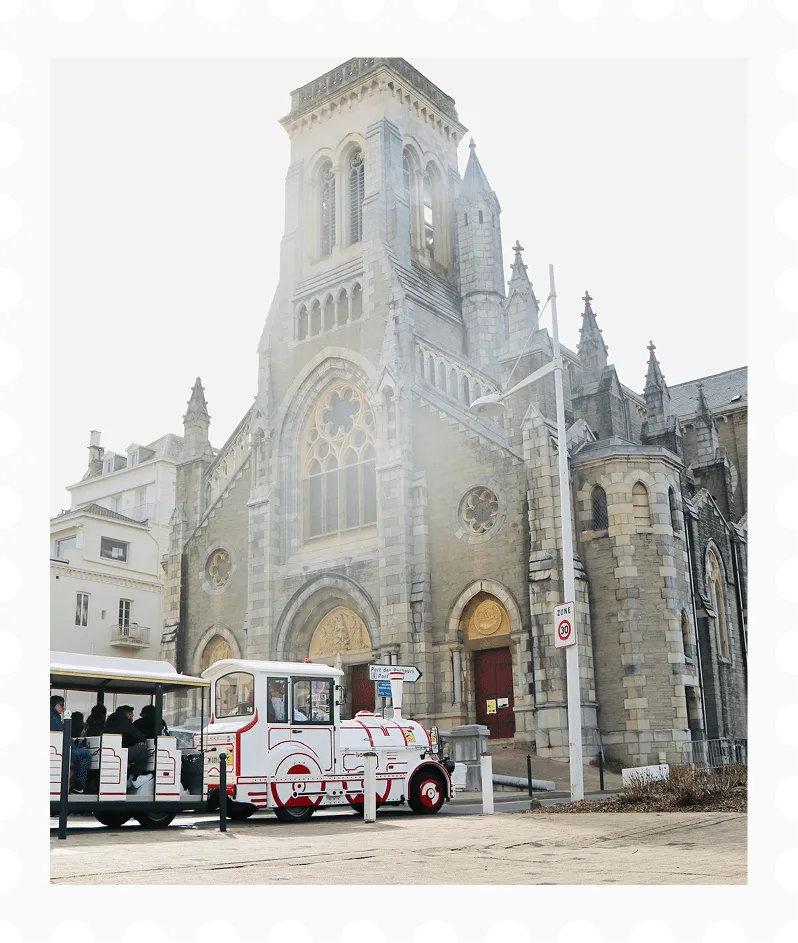 Klein toeristentreintje met passagiers, geparkeerd voor een historische stenen kerk met glas-in-loodramen en een hoge toren.