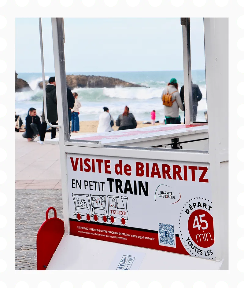 Bord dat reclame maakt voor een rondrit met het treintje in Biarritz, met strand en mensen op de achtergrond.